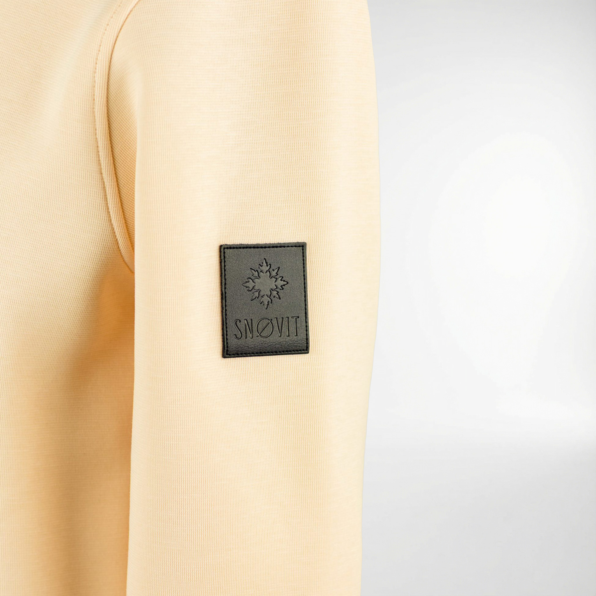 Nahaufnahme des einzigartigen SNØVIT Lederpatches auf dem beigen Sweatshirt Phantom Nebula.