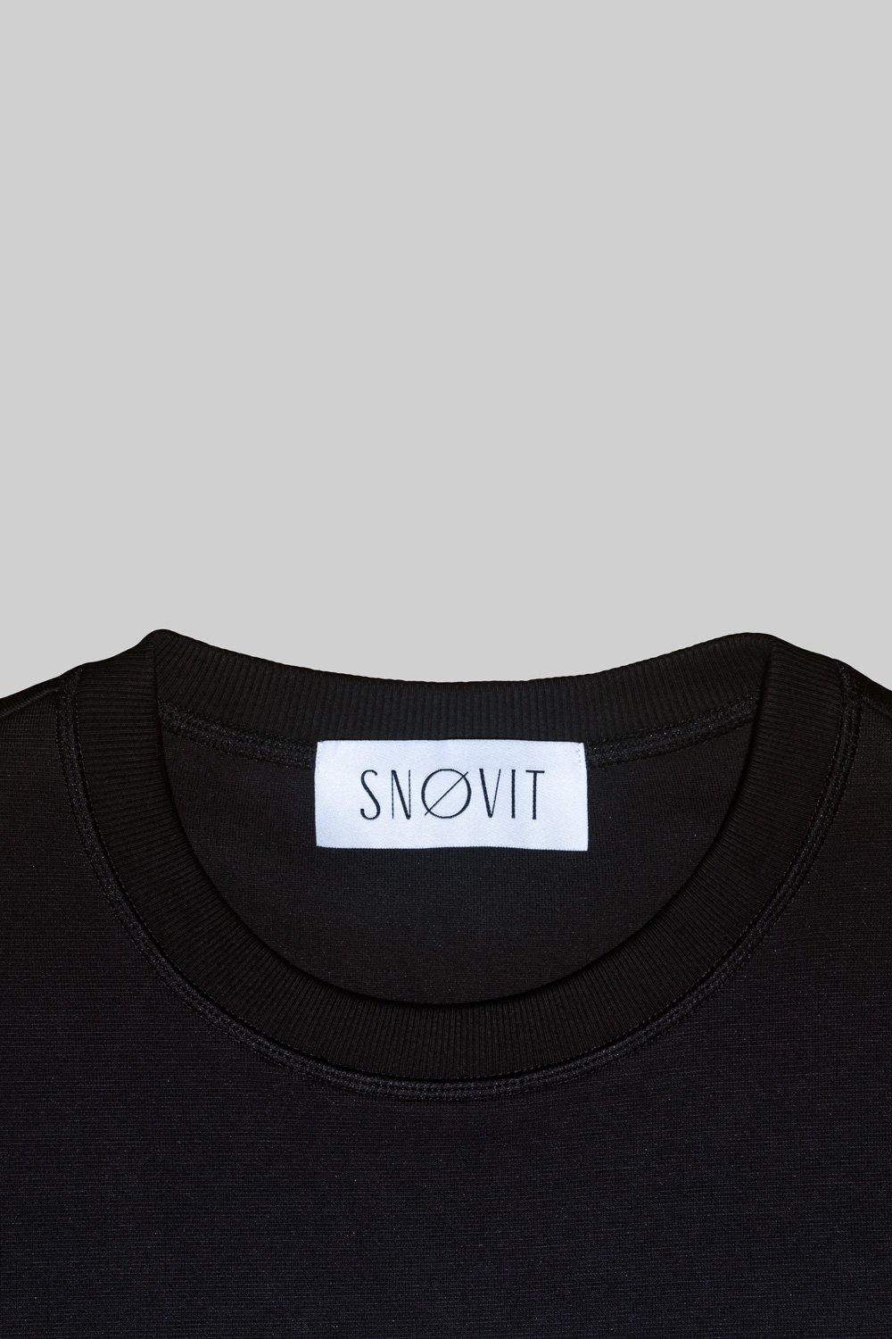 Nahaufnahme des schwarzen SNØVIT Brand-Tags im Midnight Cøre Sweatshirt, Details des Stoffes sichtbar.