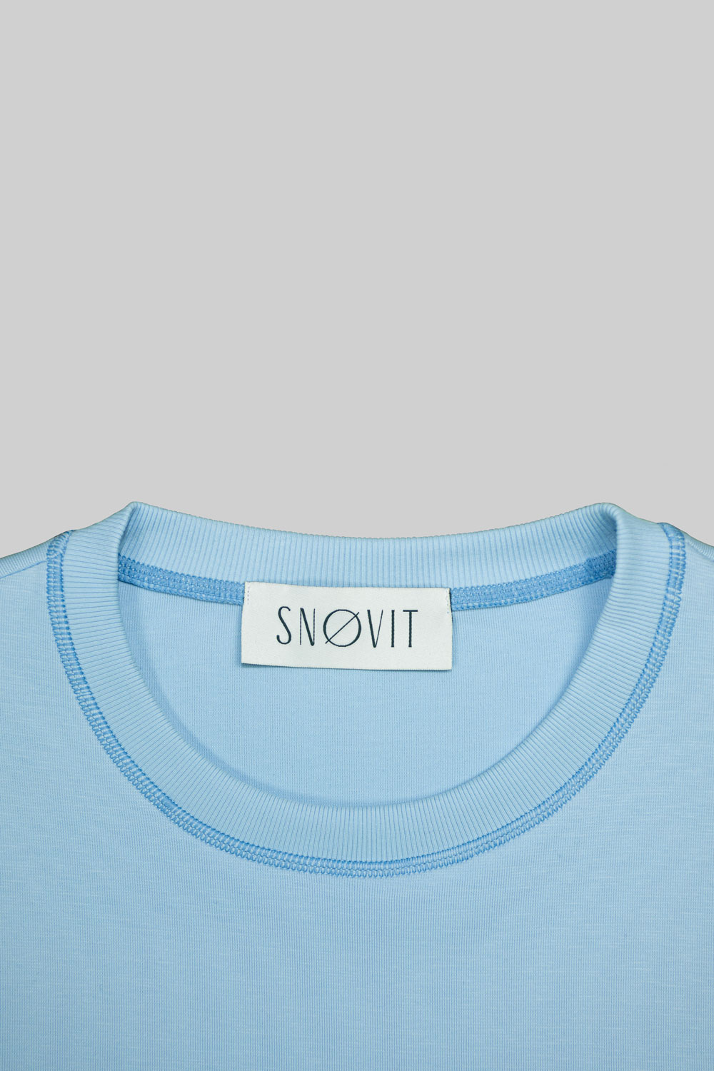 Nahaufnahme des blauen SNØVIT Brand-Tags im Deep Horizon Sweatshirt, Details des Stoffes sichtbar.