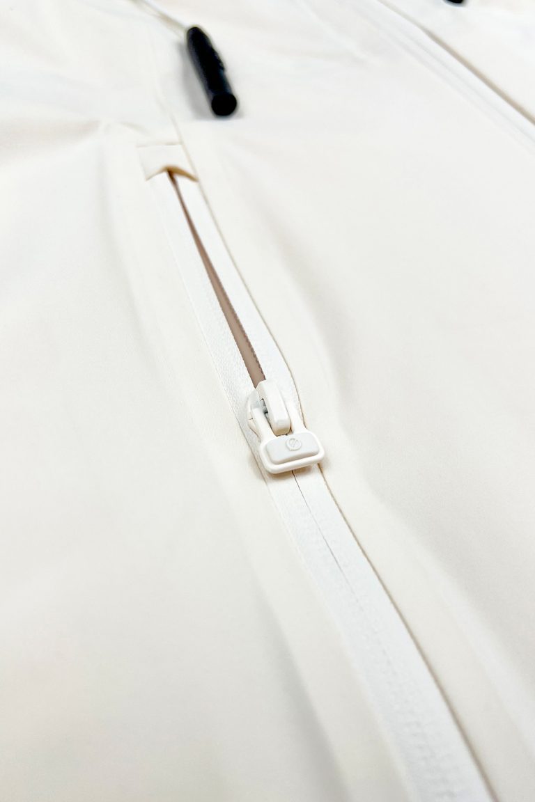 Nahaufnahme des Ø-Zippers als Zughilfe an der beige SNØVIT Moonlighter X Outdoor-Jacke für einfaches Öffnen und Schließen.