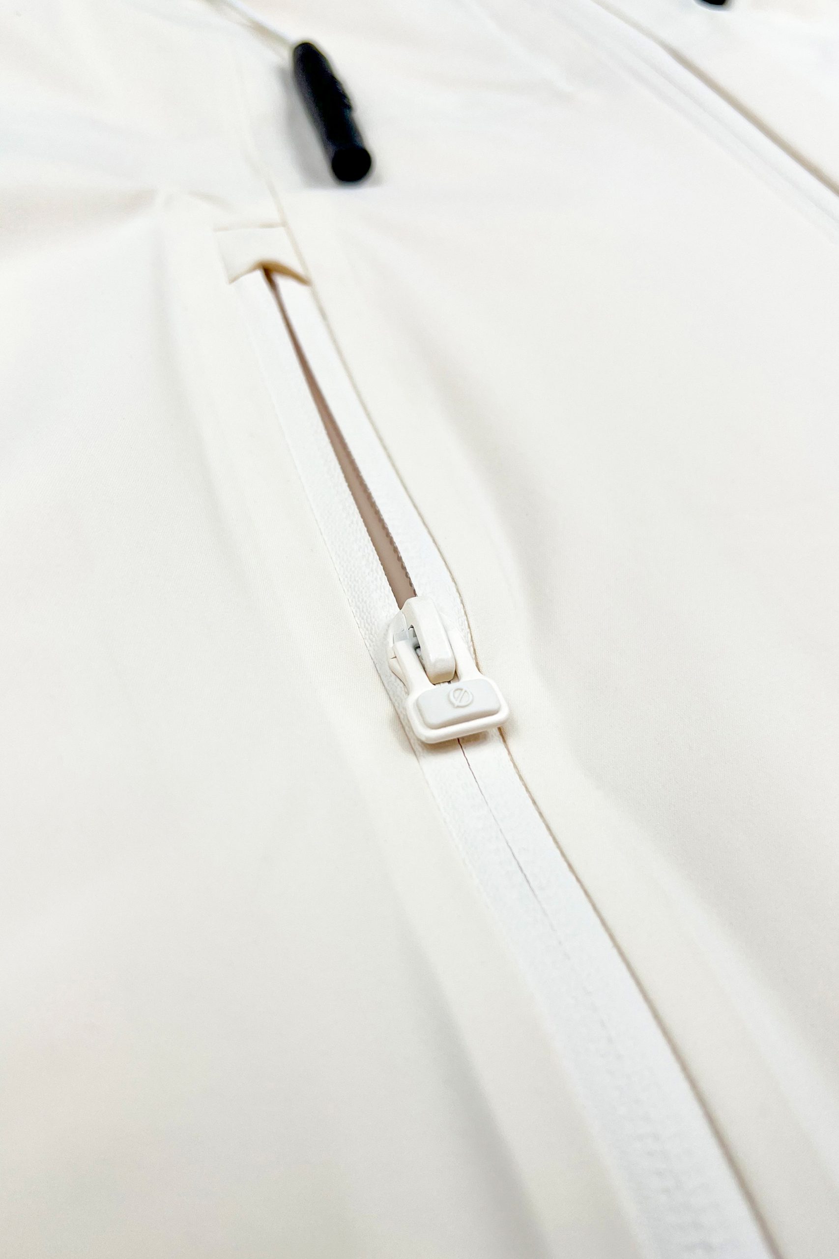 Nahaufnahme des Ø-Zippers als Zughilfe an der beige SNØVIT Moonlighter X Outdoor-Jacke für einfaches Öffnen und Schließen.