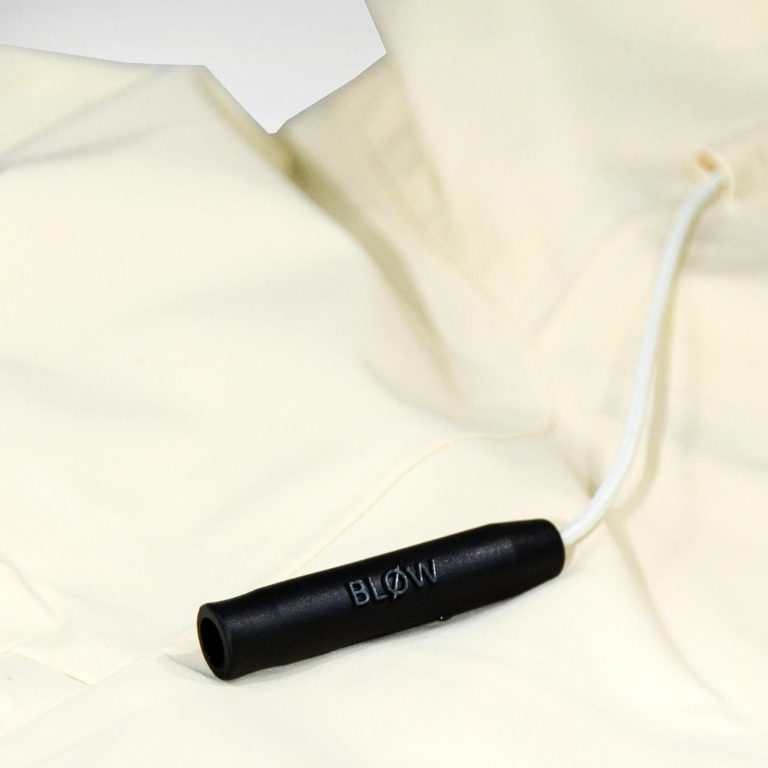 Nahaufnahme der BLØW Notfallpfeife an der beige SNØVIT Moonlighter X Outdoor-Jacke, inspiriert vom alpinen Murmeltier.