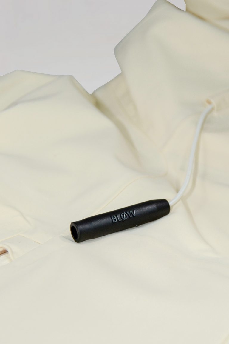 Nahaufnahme der BLØW Notfallpfeife an der beige SNØVIT Moonlighter X Outdoor-Jacke, inspiriert vom alpinen Murmeltier.