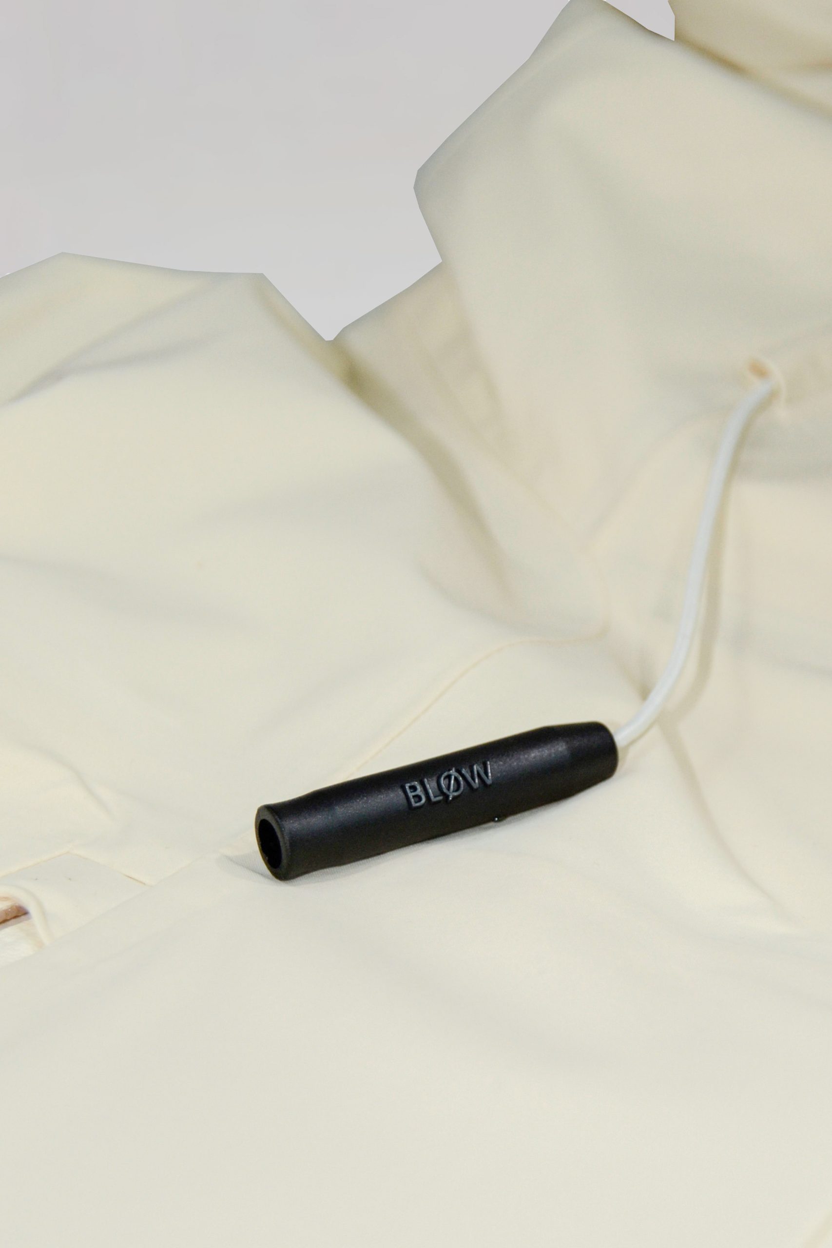 Nahaufnahme der BLØW Notfallpfeife an der beige SNØVIT Moonlighter X Outdoor-Jacke, inspiriert vom alpinen Murmeltier.