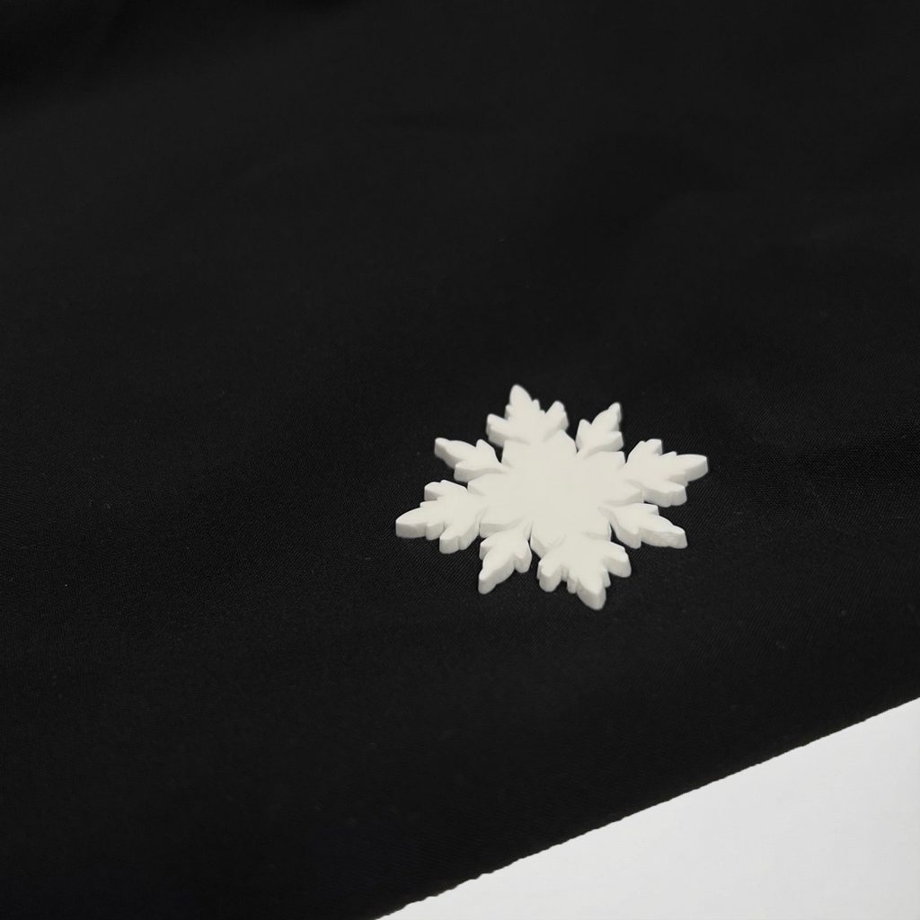 Nahaufnahme des hochwertigen weißen Schneeflocken-Rubber-Logos auf der schwarzen Nithya Nøva X Outdoor-Jacke von SNØVIT.