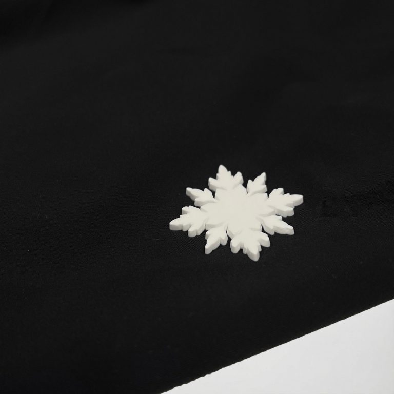 Nahaufnahme des hochwertigen weißen Schneeflocken-Rubber-Logos auf der schwarzen Nithya Nøva X Outdoor-Jacke von SNØVIT.