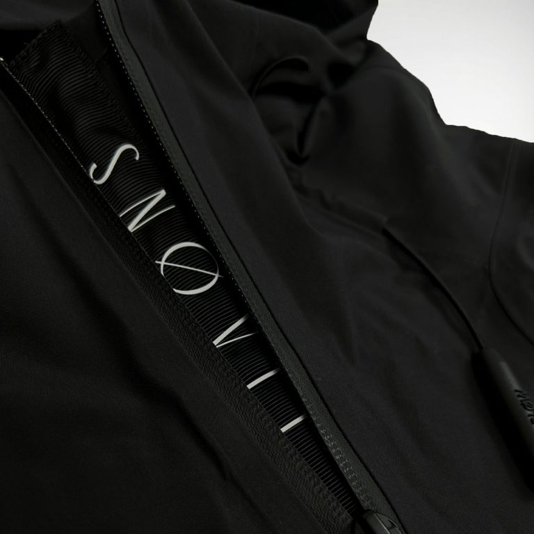 Nahaufnahme des gewebten SNØVIT Stripes an der schwarzen Nithya Nøva X Outdoor-Jacke, hochwertige Nylonstruktur sichtbar.