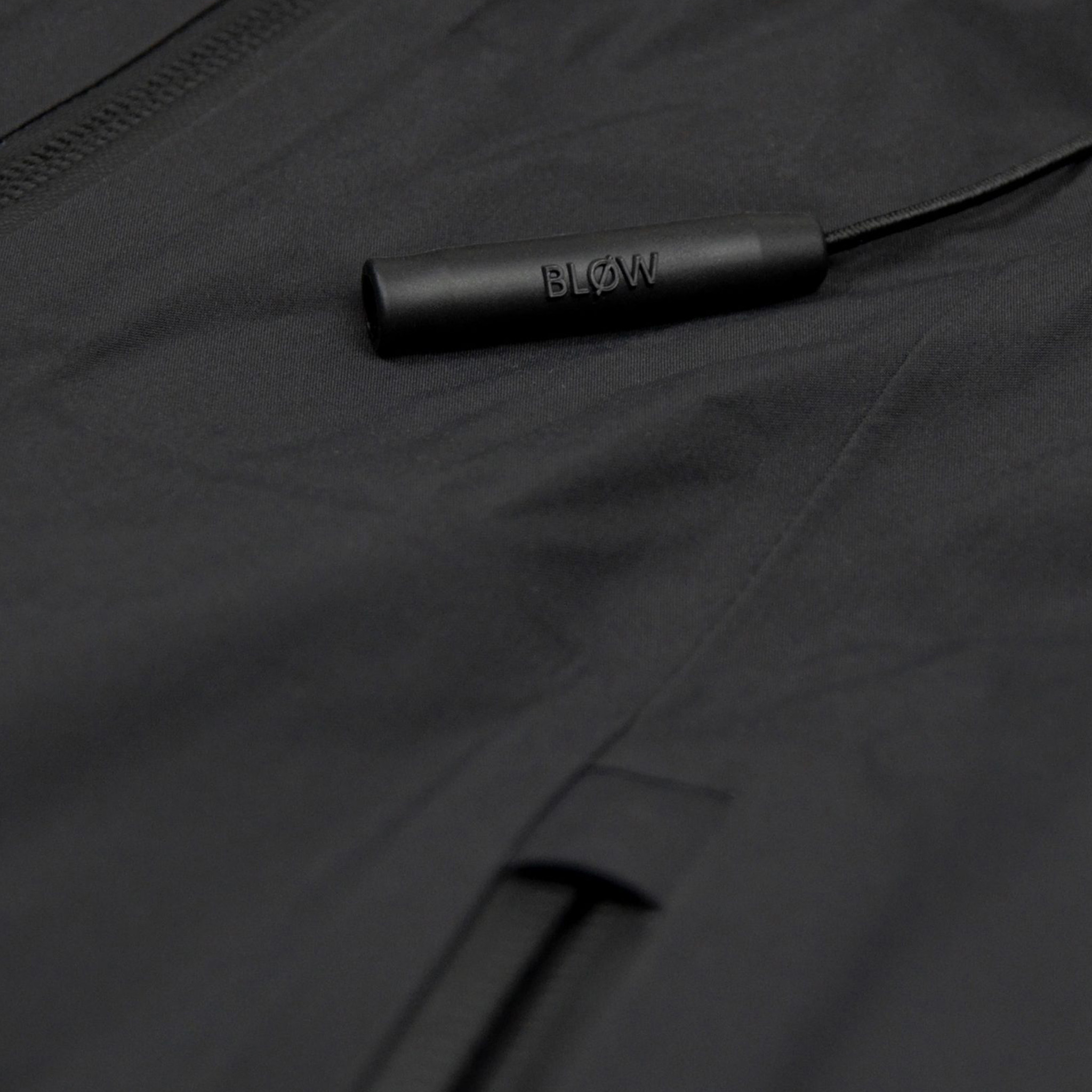 Nahaufnahme der eingebauten Notfall-Pfeife „BLØW“ an der SNØVIT Nithya Nøva X Outdoor-Jacke, inspiriert vom Alpengürtelmurmeltier.