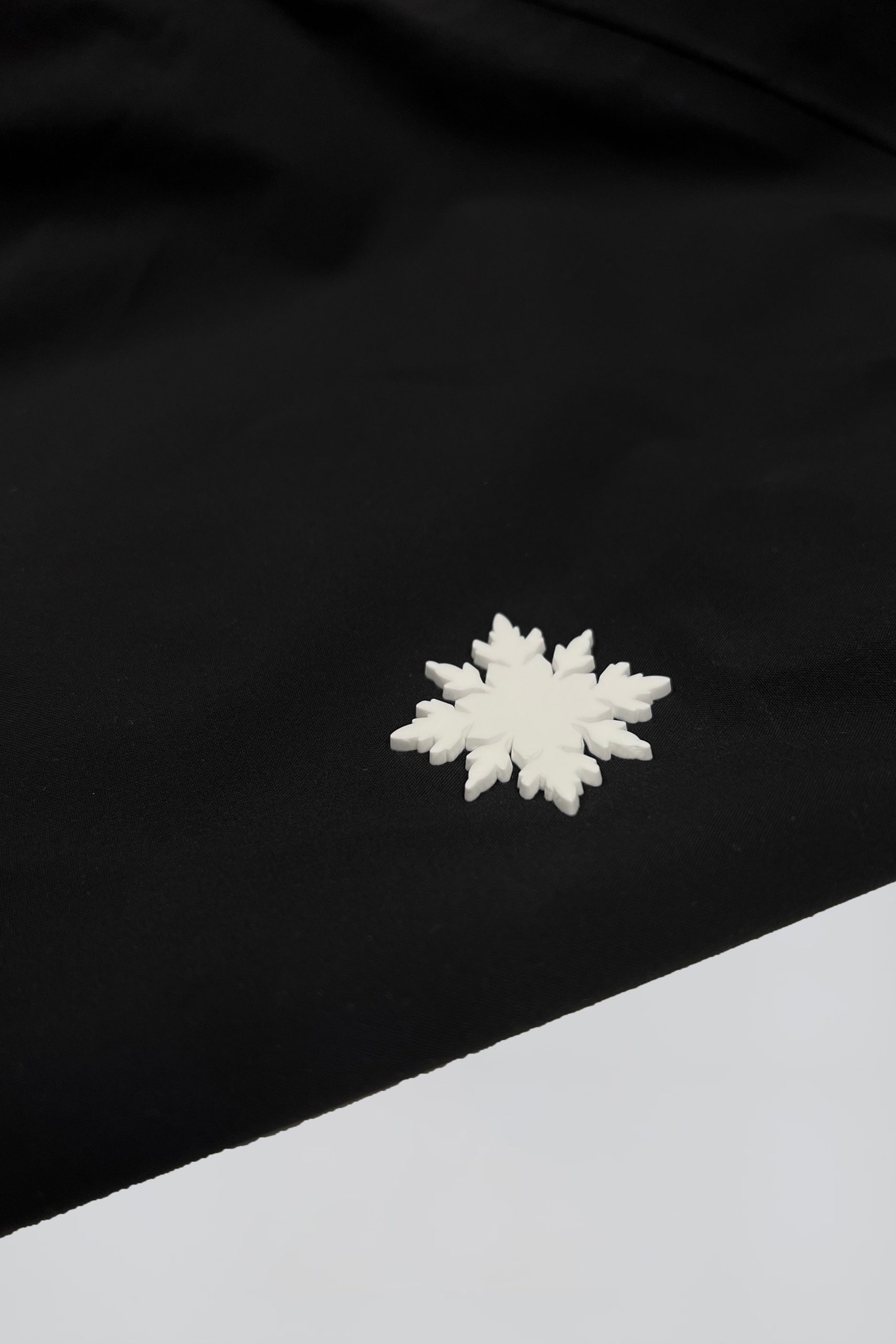 Nahaufnahme des hochwertigen weißen Schneeflocken-Rubber-Logos auf der schwarzen Nithya Nøva X Outdoor-Jacke von SNØVIT.