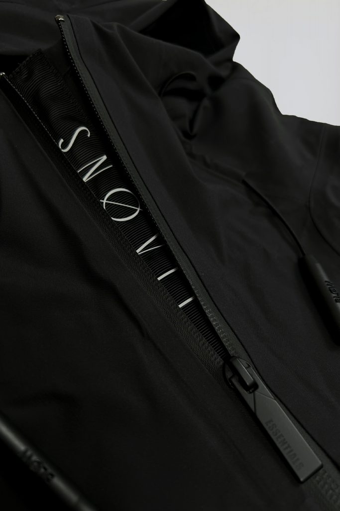 Nahaufnahme des gewebten SNØVIT Stripes an der schwarzen Nithya Nøva X Outdoor-Jacke, hochwertige Nylonstruktur sichtbar.
