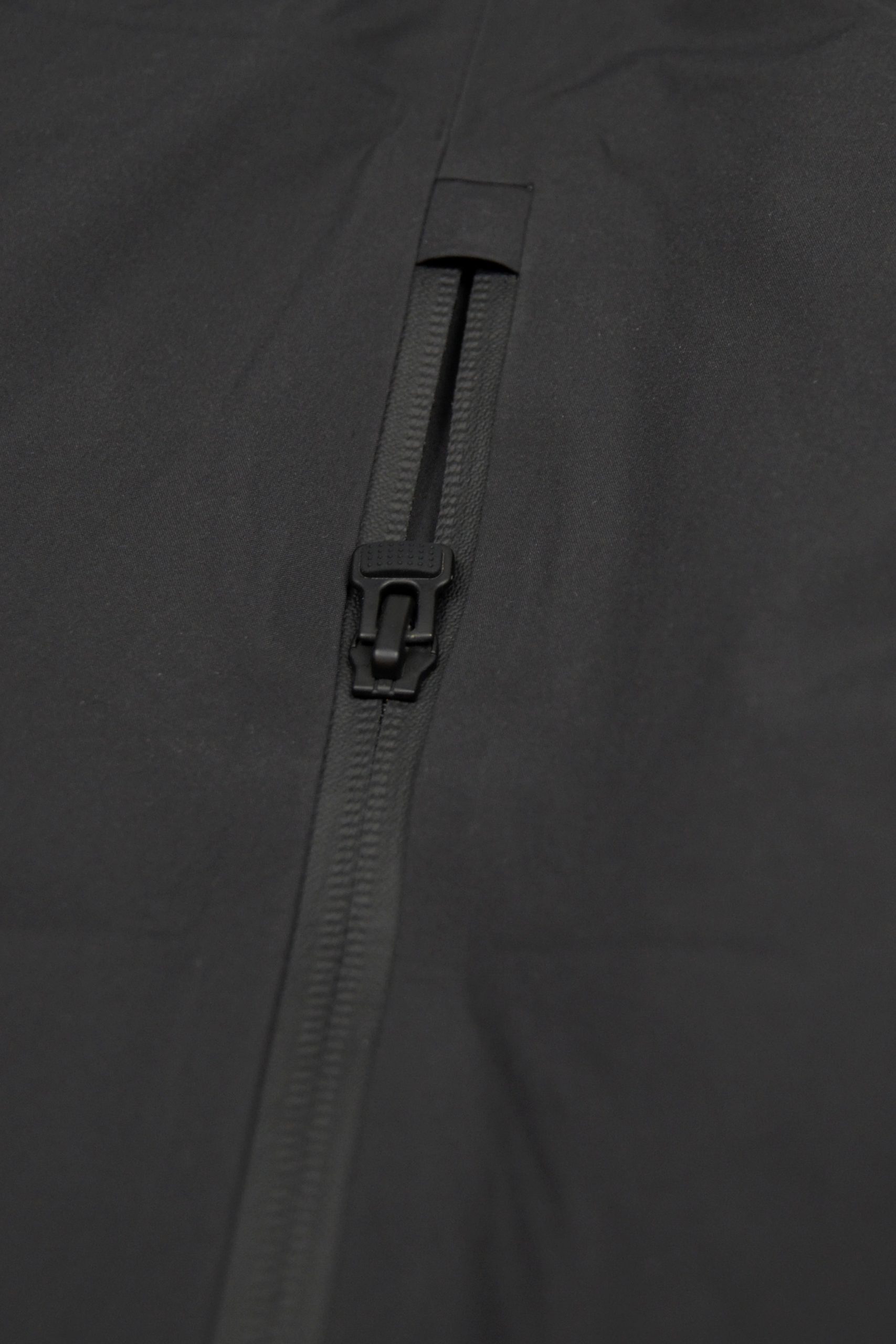 Nahaufnahme des robusten Ø-Zippers an der Rückseite der SNØVIT Nithya Nøva X Outdoor-Jacke. Das praktische Ø-Design erleichtert das Öffnen und Schließen der Taschen und steht für höchste Verarbeitungsqualität.