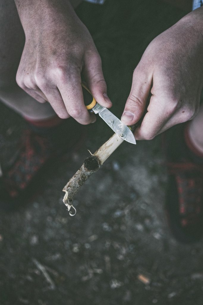 Person schnitzt entspannt Holz mit einem Messer im Wald, 1988.