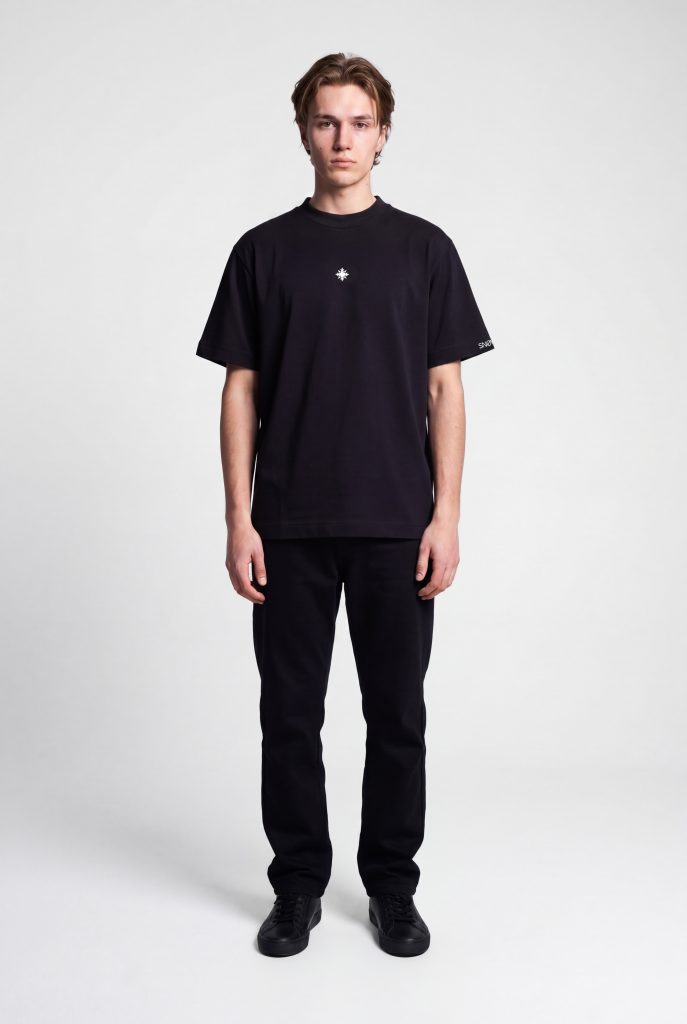 Model trägt schwarzes SNØVIT Eclipse T-Shirt im Produktstudio – minimalistisches Design, 100 % Baumwolle, moderne Passform, zeitloses Basic.