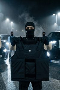 Maskierter Model hält die schwarze defenx pro vanta weste in die kamera. Stichfeste panele